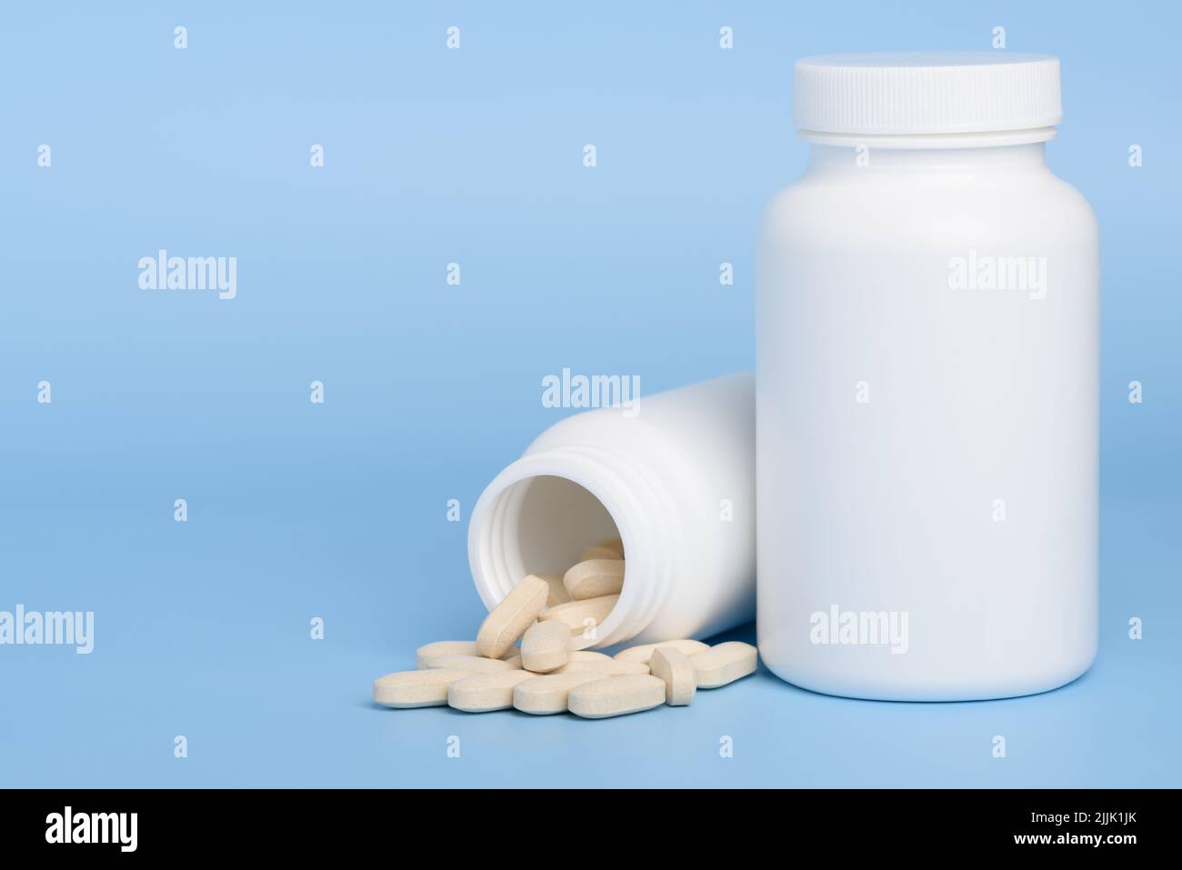 Two white medicine bottles, one closed and second with pills spilled on blue background with copy-space Stock Photo
