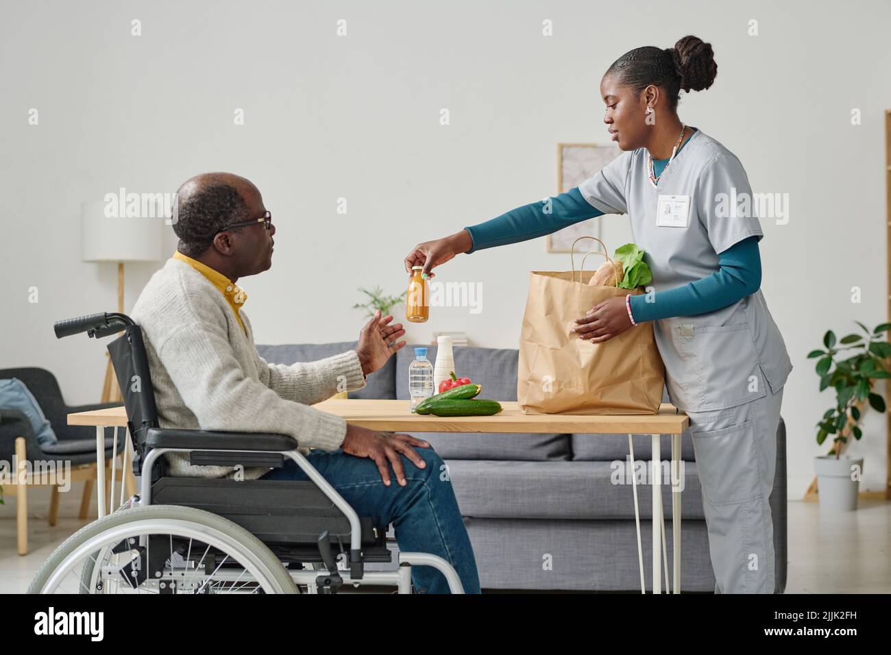 African young caregiver unpacking shopping bag with food she delivering
