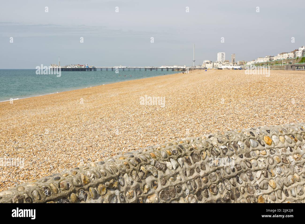 Shingle beach at Brighton in East Sussex, England. Viewed from near Marina with pier in background. Unrecognisable people relaxing on beach. Stock Photo