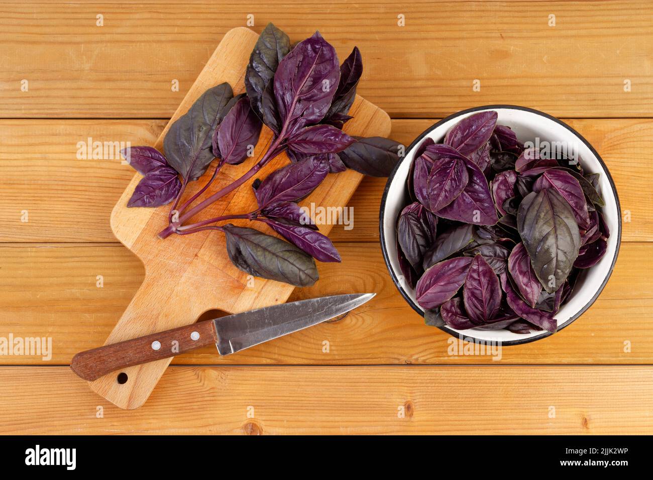 Purple basil leaves on the cutting board and in a bowl on a wooden kitchen table. Top view. Stock Photo