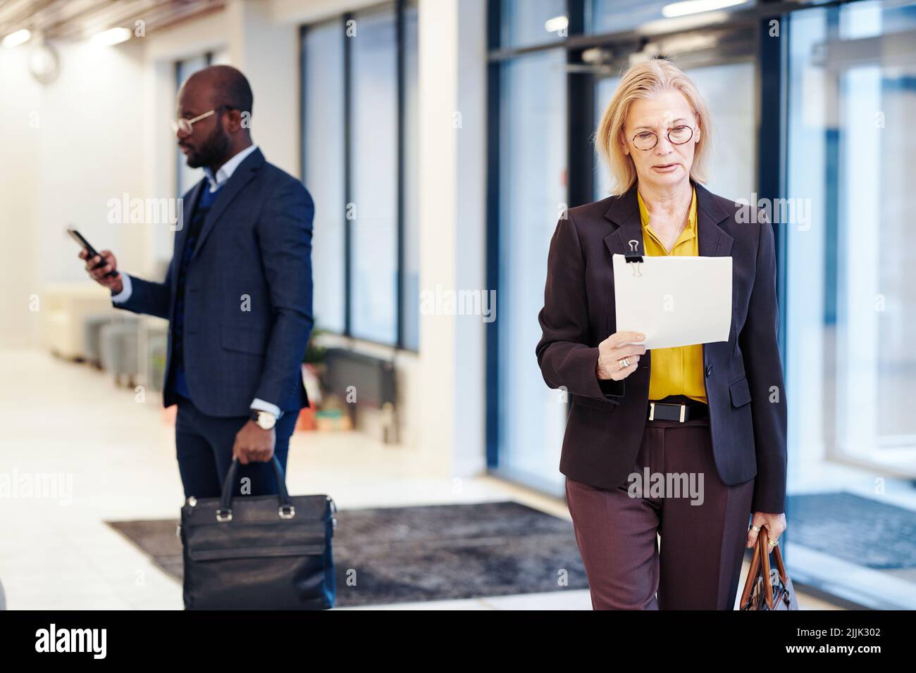 Mature female lawyer reading the document while walking along the street outdoors, she leaving the courtroom Stock Photo