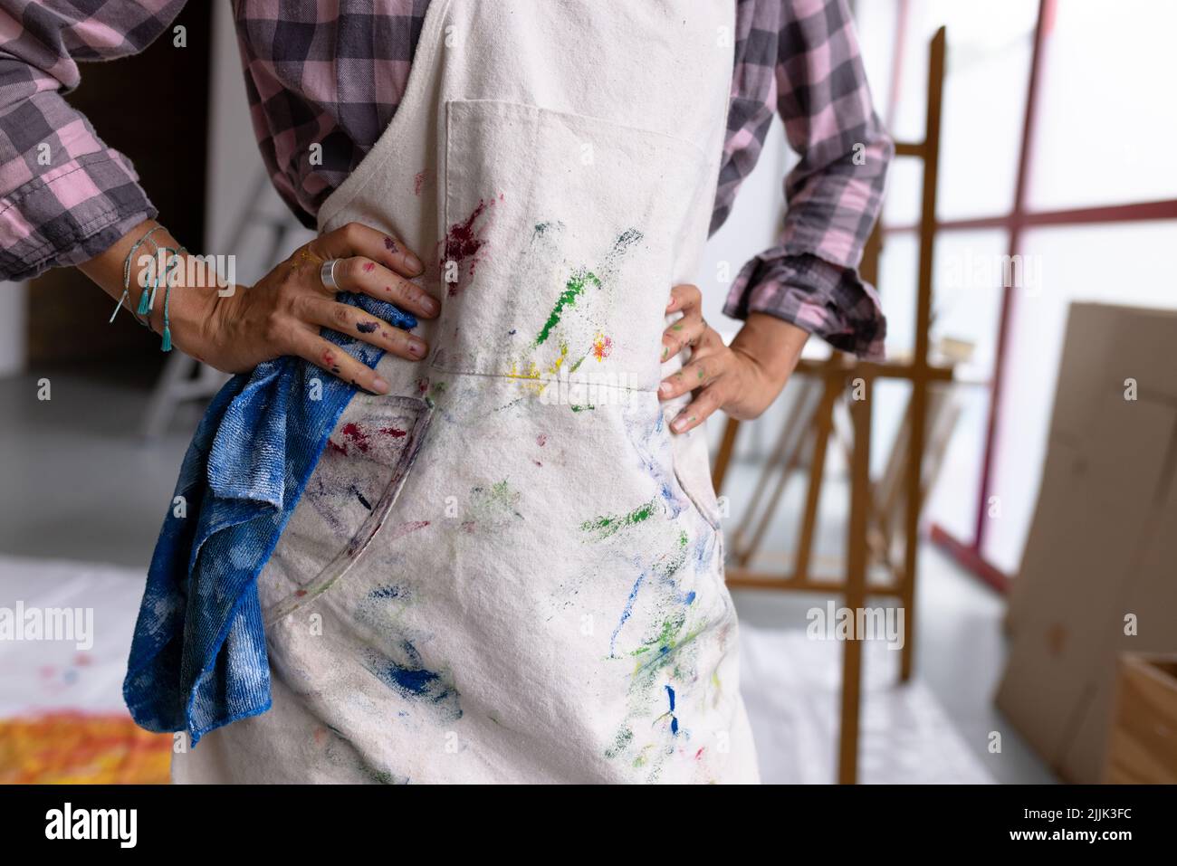 Image of midsection of biracial female artist in painted apron in studio Stock Photo