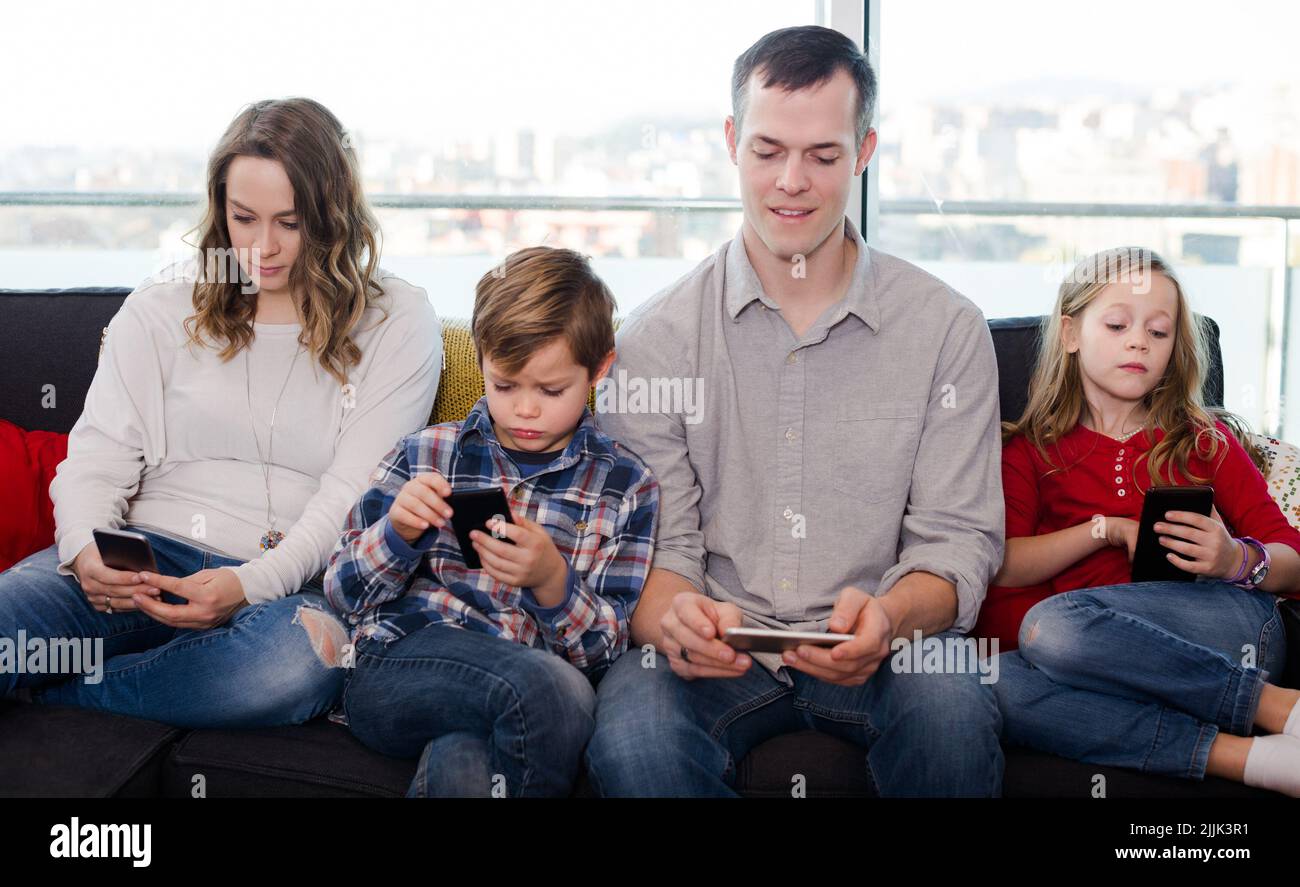Cheerful family members spending time playing with smartphones Stock Photo