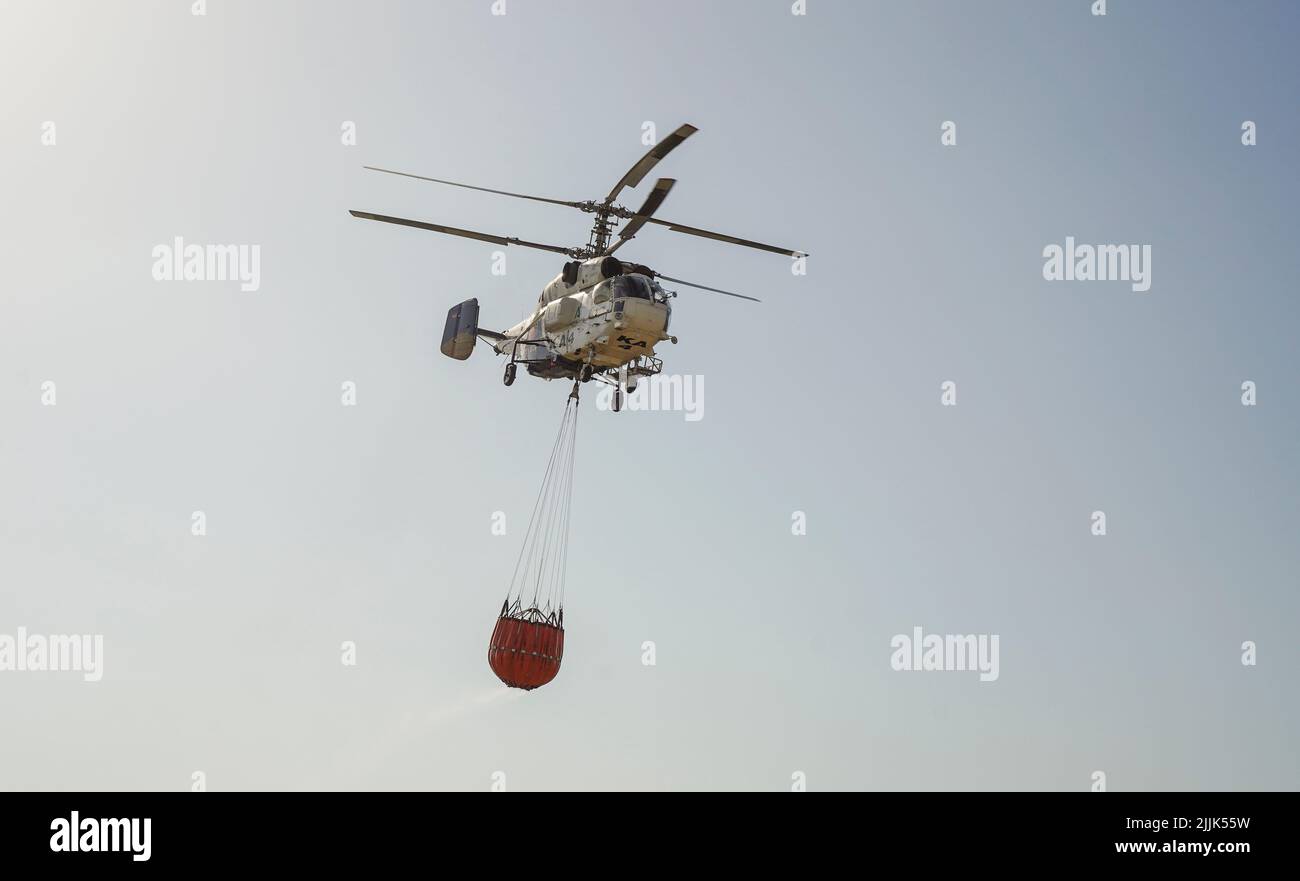 Heavy helicopter of INFOCA carrying a water bucket to drop on a wildfire, Mijas, Spain. Stock Photo