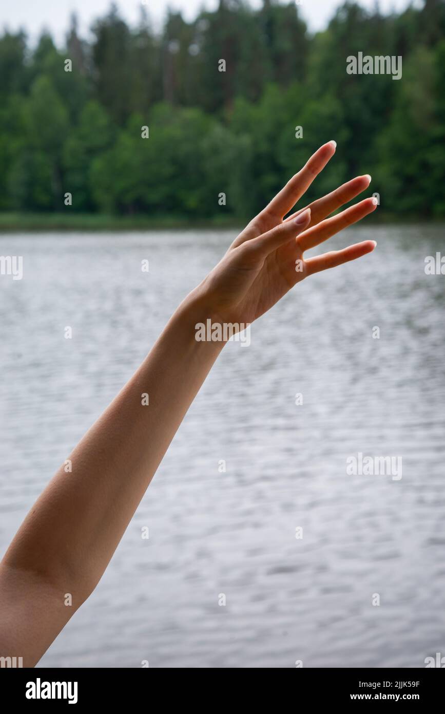 Close up of female hand in blue sleeve raised up over blue sky and clouds background. Women's hands reach for the sky. People, childhood, gesture and Stock Photo