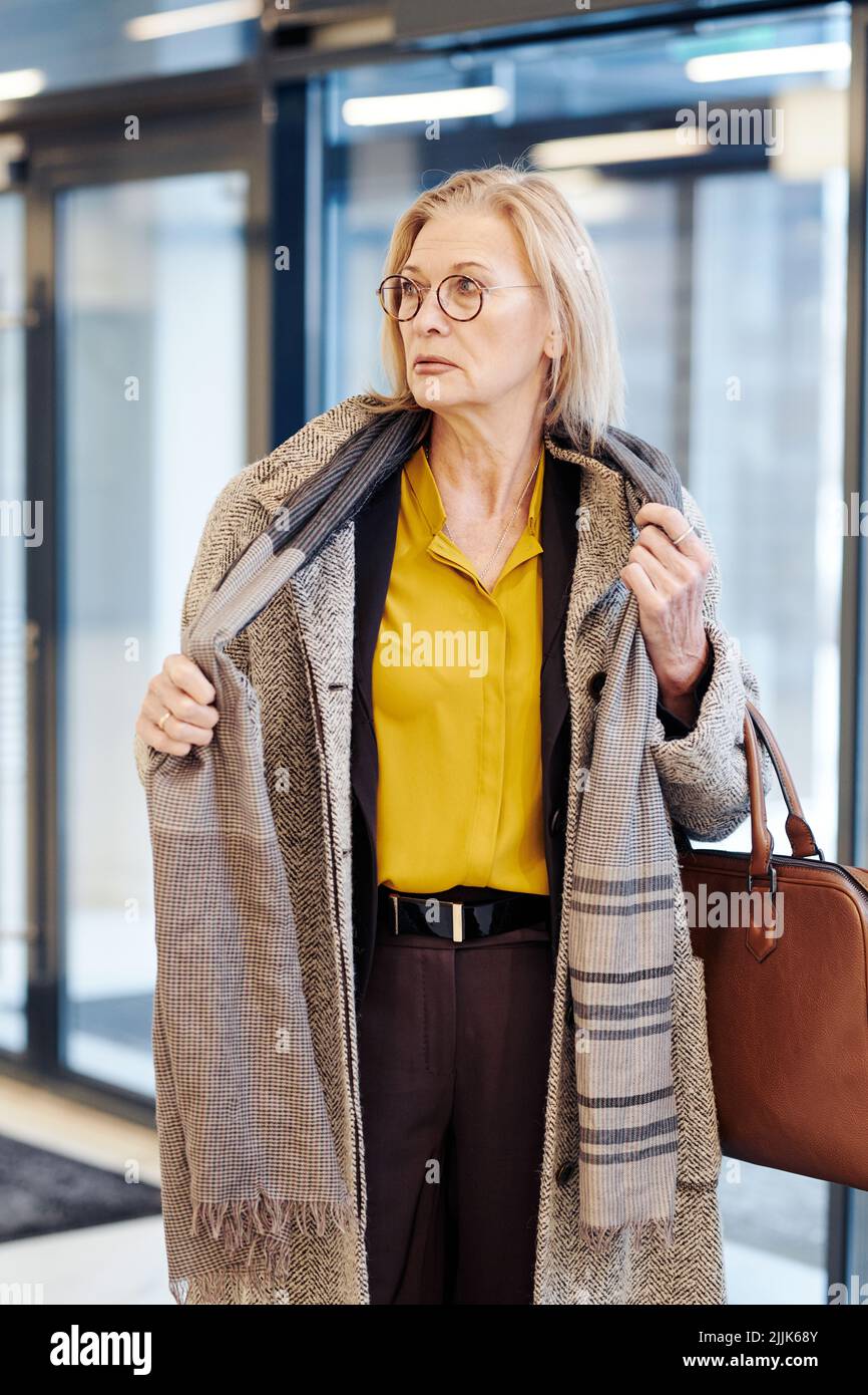 Serious mature lawyer taking off the warm coat while entering in the courthouse for meeting Stock Photo