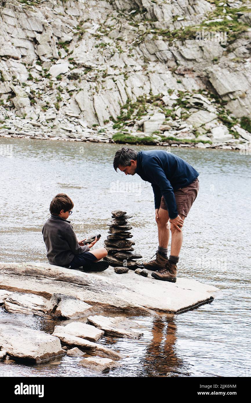 A vertical shot of a man and his son stacking pebbles on the lake shore in France Stock Photo