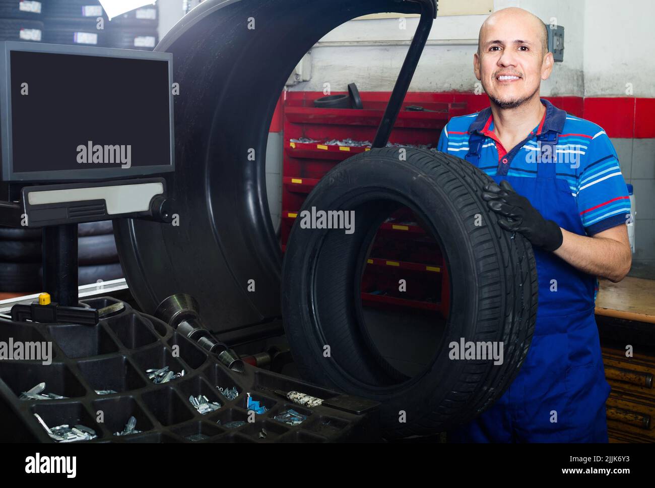 Mature male technician holding car wheel ready to work with balancing machinery at workshop Stock Photo