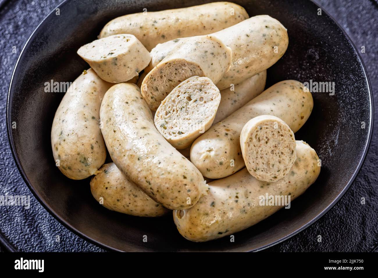 Weisswurst, bavarian white sausages of minced veal, pork back bacon, spices and parsley  in black bowl, close-up Stock Photo