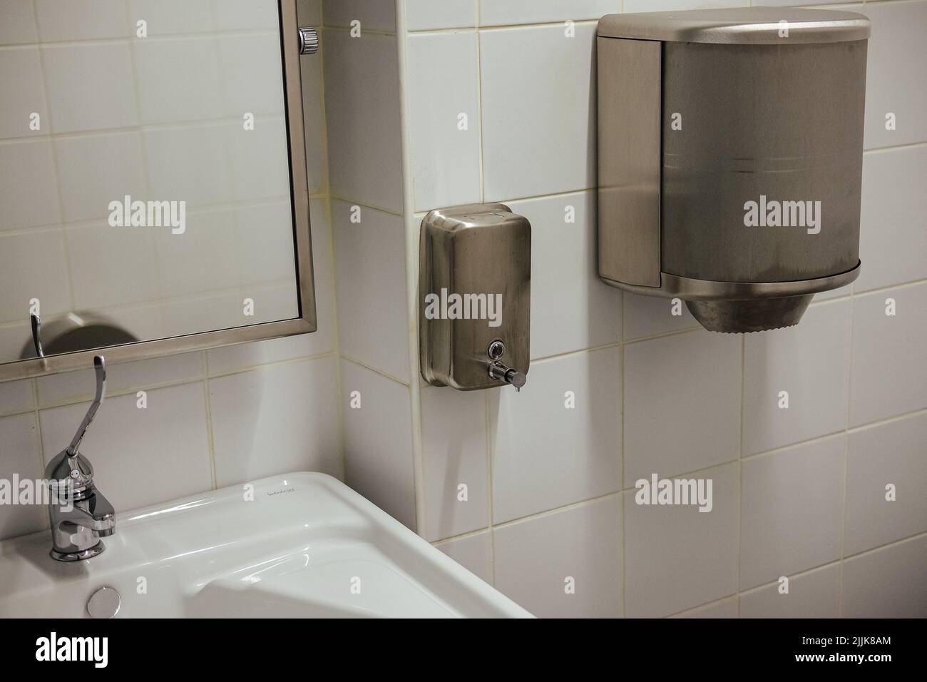 A silver soap dispenser and towel dispenser in a white tile bathroom Stock Photo
