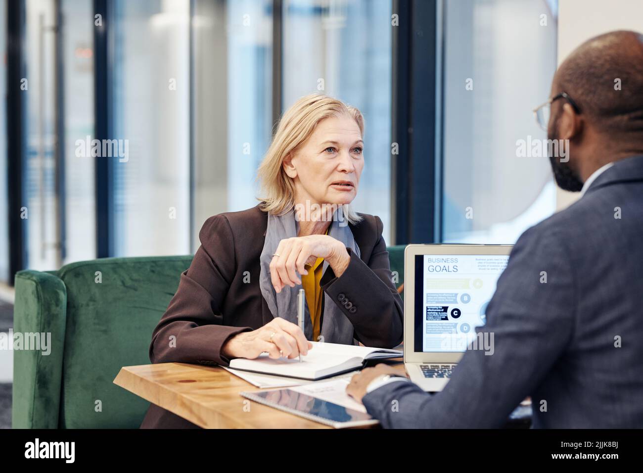 Mature female lawyer discussing the legal deal with her colleague who using the laptop, they sitting at the table at business meeting Stock Photo