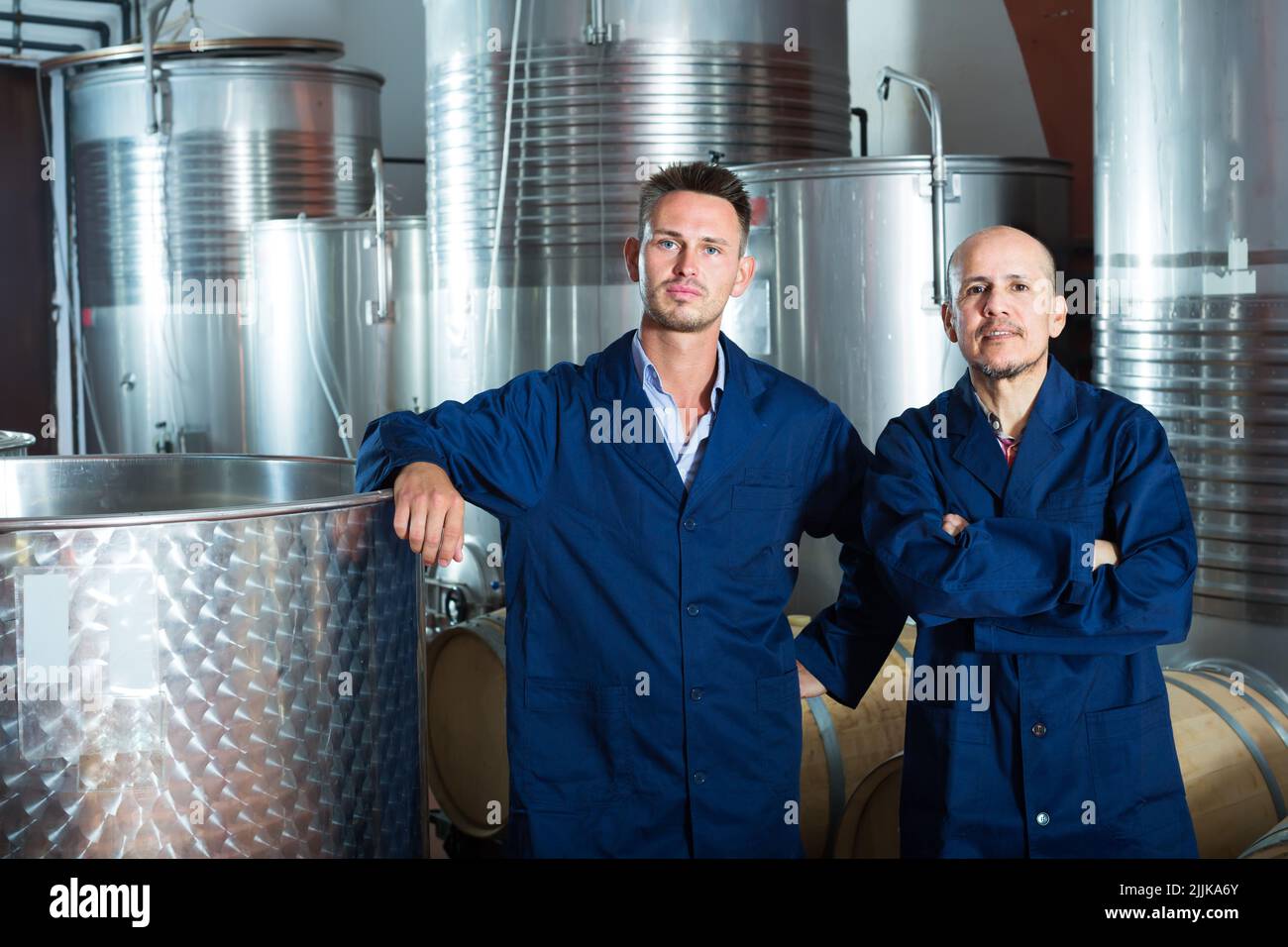 Two friendly men in uniforms standing in winery fermentation compartment Stock Photo