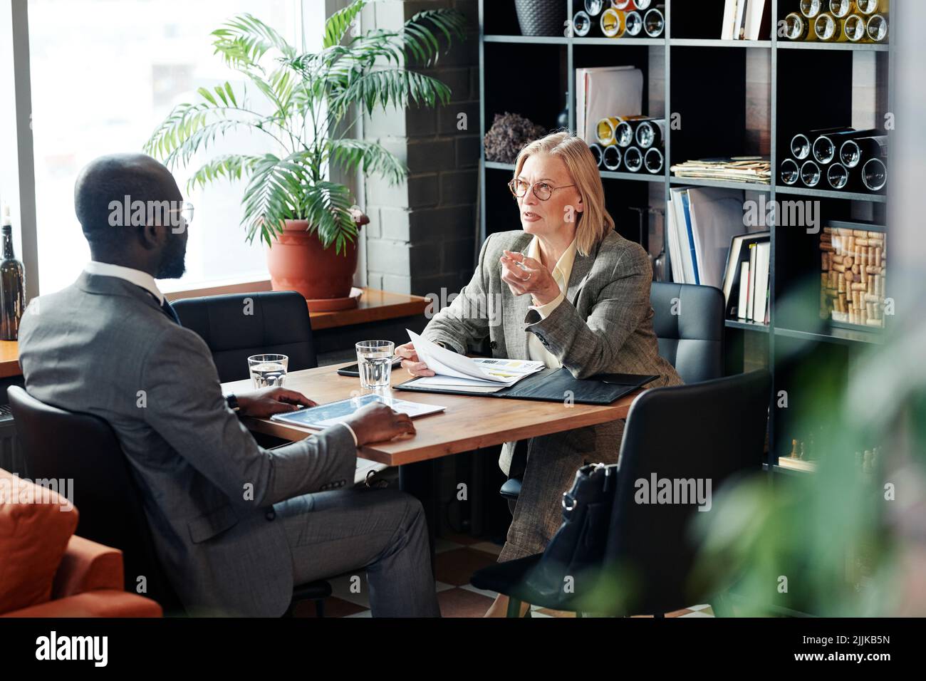 Mature businesswoman talking to African businessman at the table with documents, they discussing contract during meeting at restaurant Stock Photo