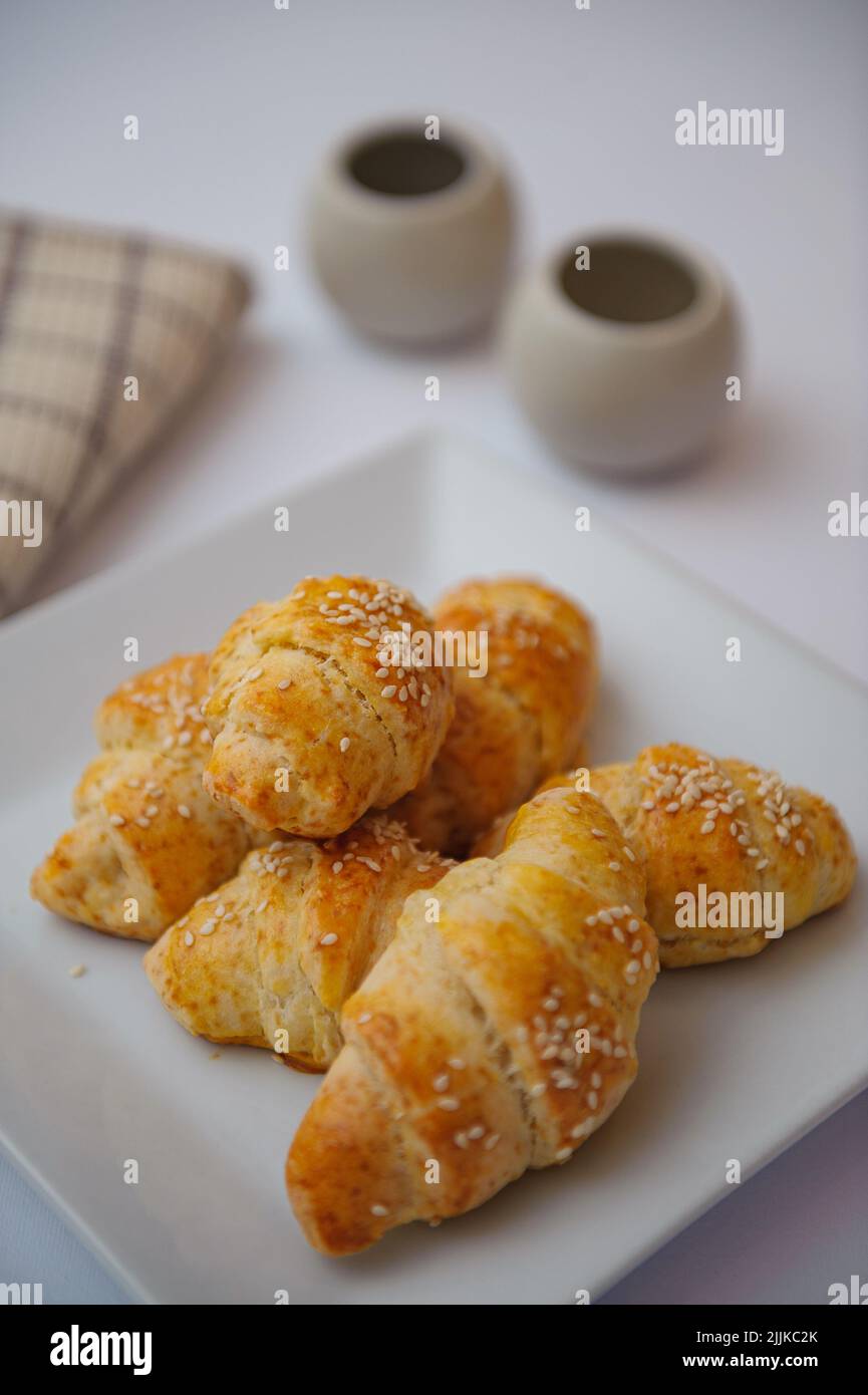 A close-up shot of croissants with cheese and sesame in white plate on a white table with blurred background Stock Photo