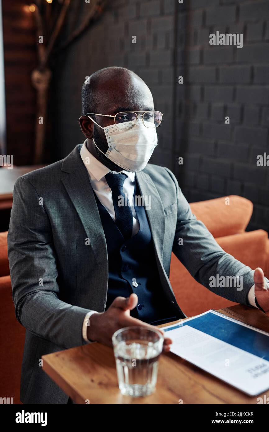 African businessman in suit wearing protective mask while having a meeting at the restaurant Stock Photo