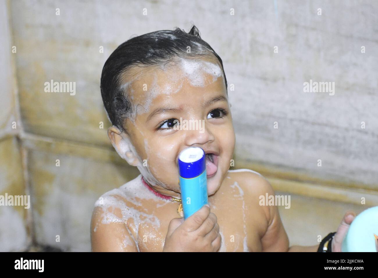 A portrait of a cheerful cute Indian baby holding a shampoo with foam all over his body taking a bath Stock Photo