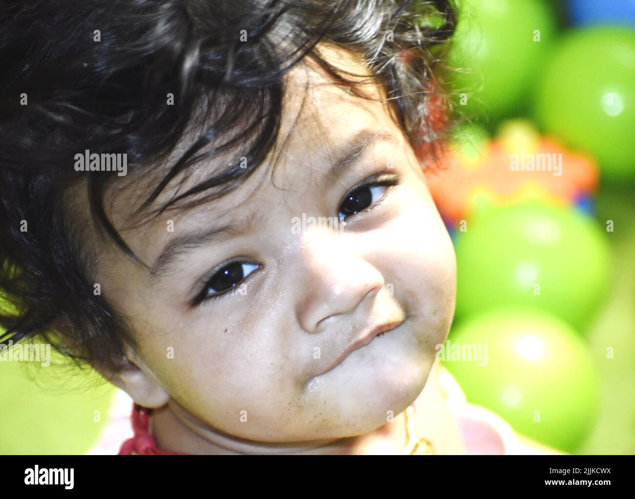 A portrait of a cute Indian baby with big eyes sitting on the playground Stock Photo