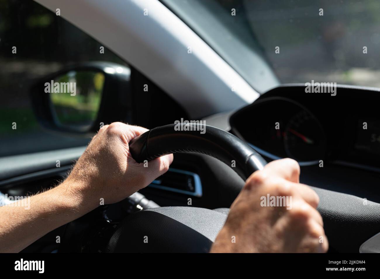 White men hands control a car steering wheel while driving on the road. There are no recognizable persons or trademarks in the shot. Stock Photo