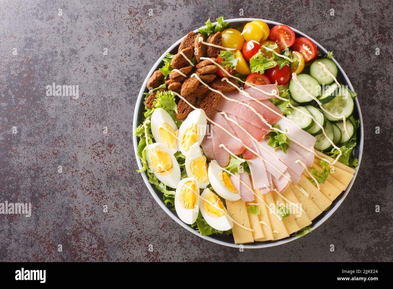 American hearty chef salad of vegetables, lettuce, eggs, cheese, croutons and several types of meat close-up in a plate on the table. horizontal top v Stock Photo