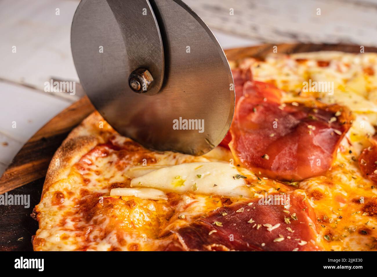 A metallic pizza roll cutter cutting a Spanish Iberian ham pizza Stock