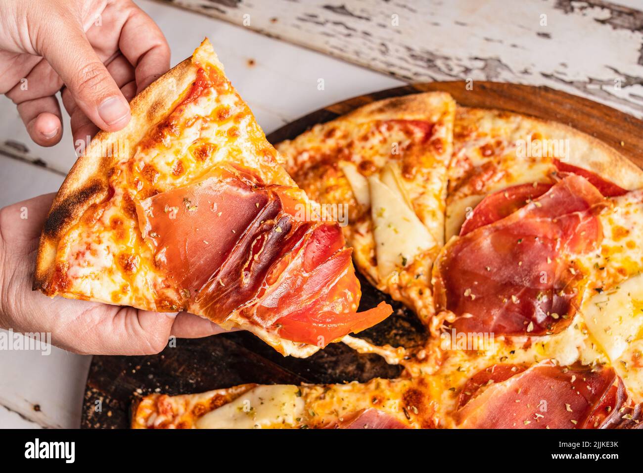 A hand picking a piece of Spanish Iberian ham pizza Stock Photo - Alamy