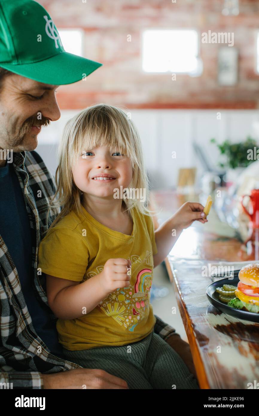 A closeup of a cute little girl with his dad ready to eat her hamburger Stock Photo