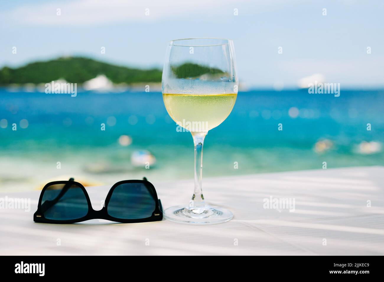 A closeup of a glass of cold white wine and sunglasses with beach on background Stock Photo