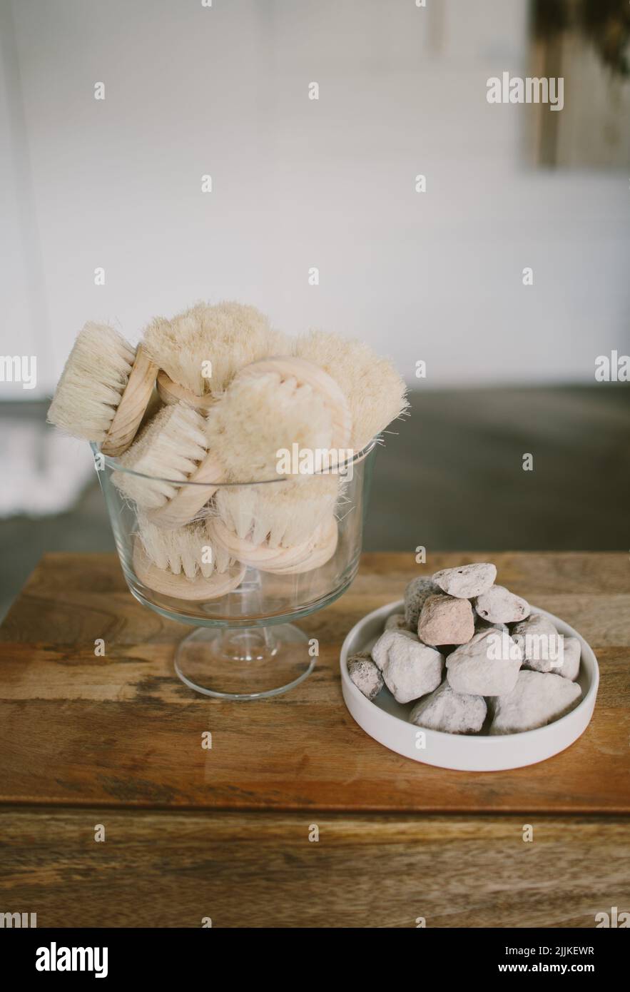 A vertical shot of massaging brushes in a glass next to some stones on a plate on a wooden table. Stock Photo