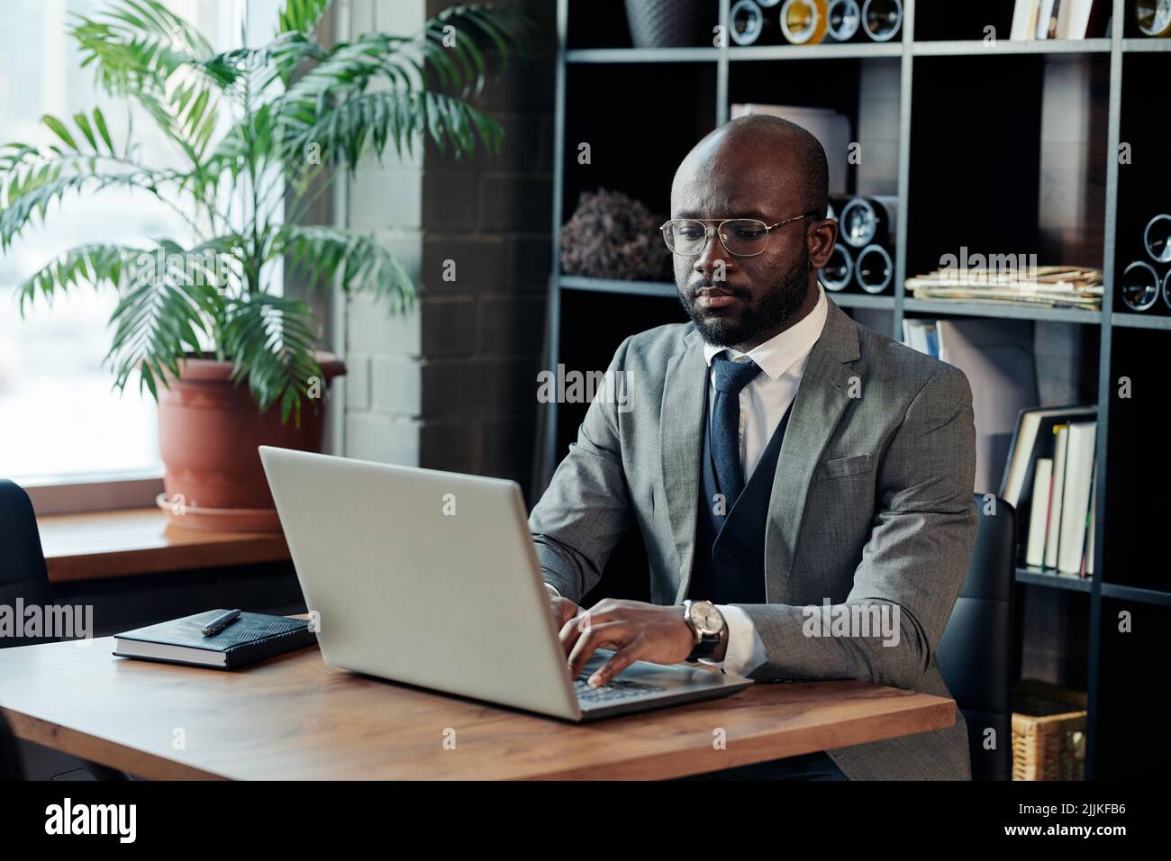 African businessman in suit sitting at the table and typing on laptop, he working online at the restaurant Stock Photo