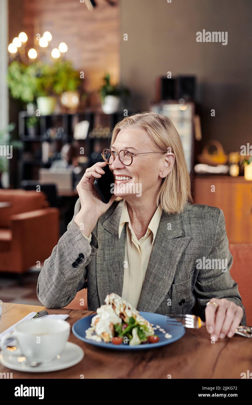 Successful mature businesswoman smiling while having conversation on mobile phone during her lunch at the restaurant Stock Photo