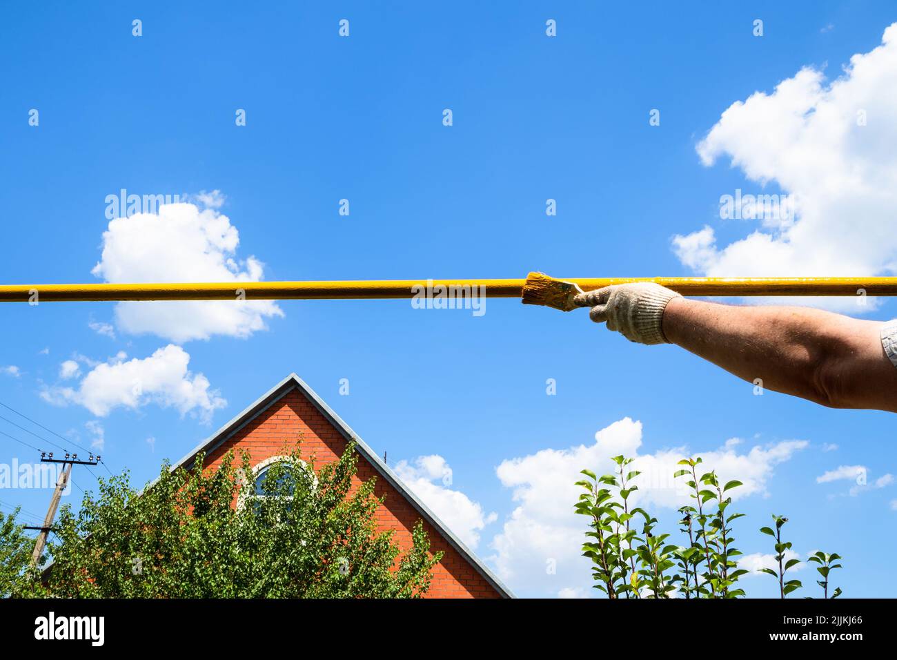 painting outdoor gas pipe with yellow paint using brush in village on