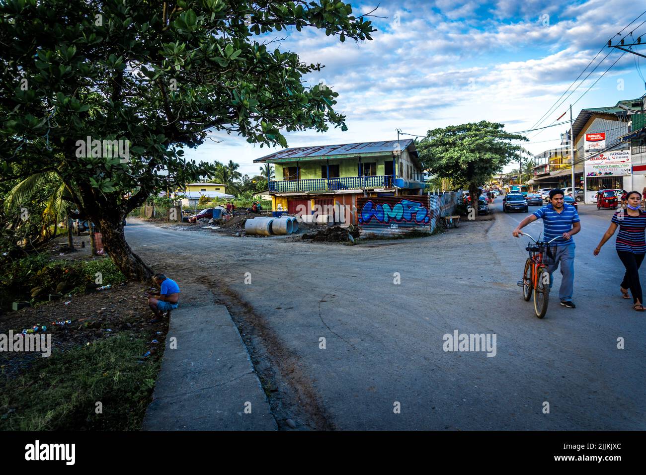 A shot of people walking and riding a bicycle on the crossroad against the colorful buildings in Costa Rica Stock Photo