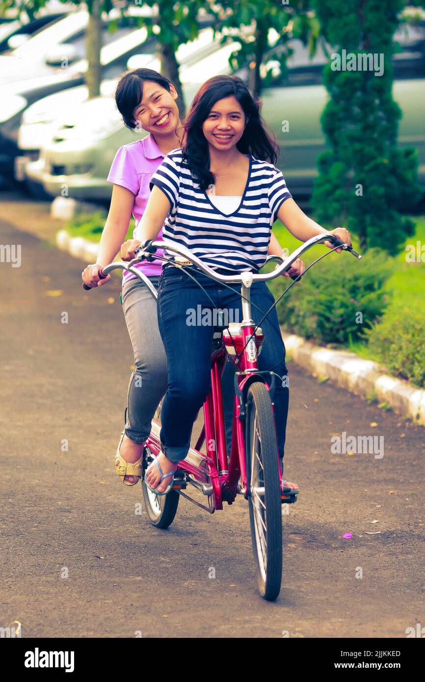 Portrait of young and beautiful Asian girls on tandem bicycle ride in street. Smiling happy and fun expression. For friendship and together concept. Stock Photo