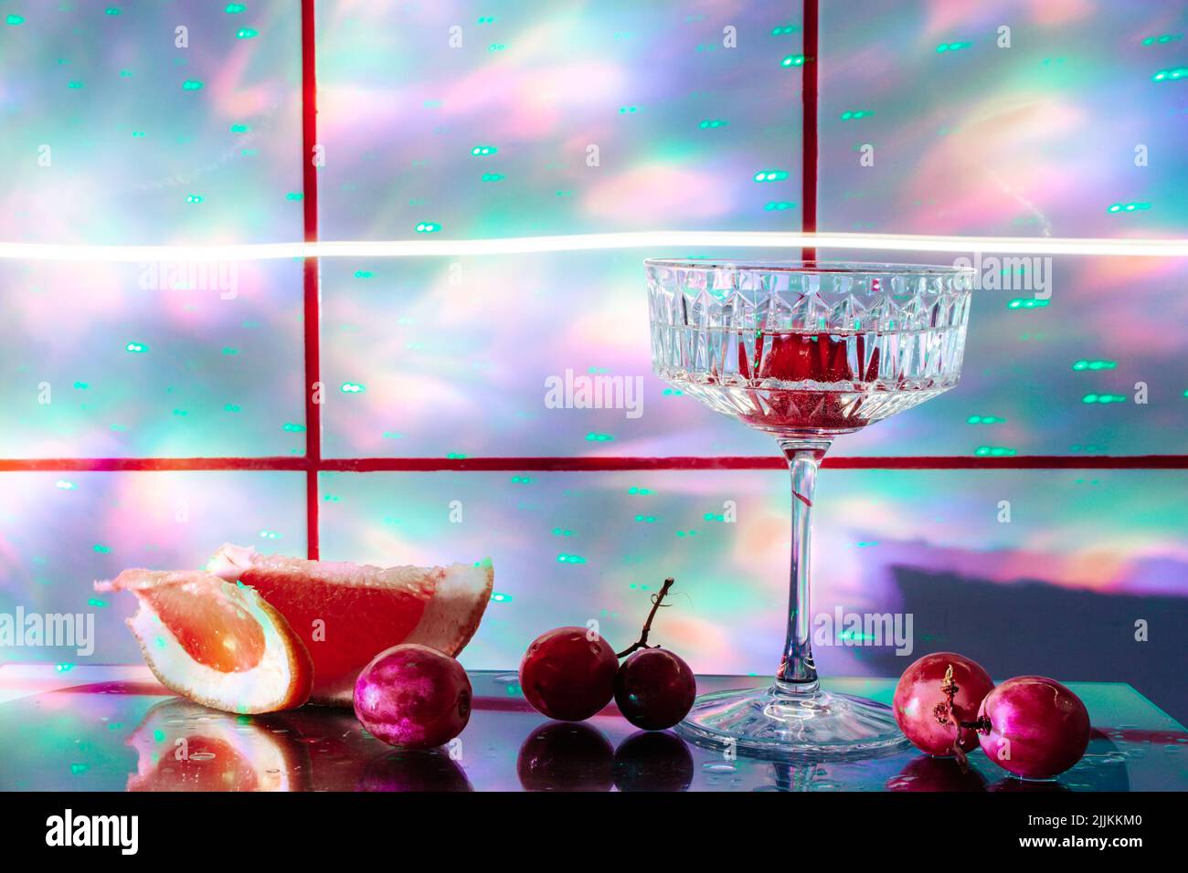 Crystal glass for cocktails on a glass surface. Fruits - grapes, grapefruit  next to the glass. Abstract background Stock Photo - Alamy