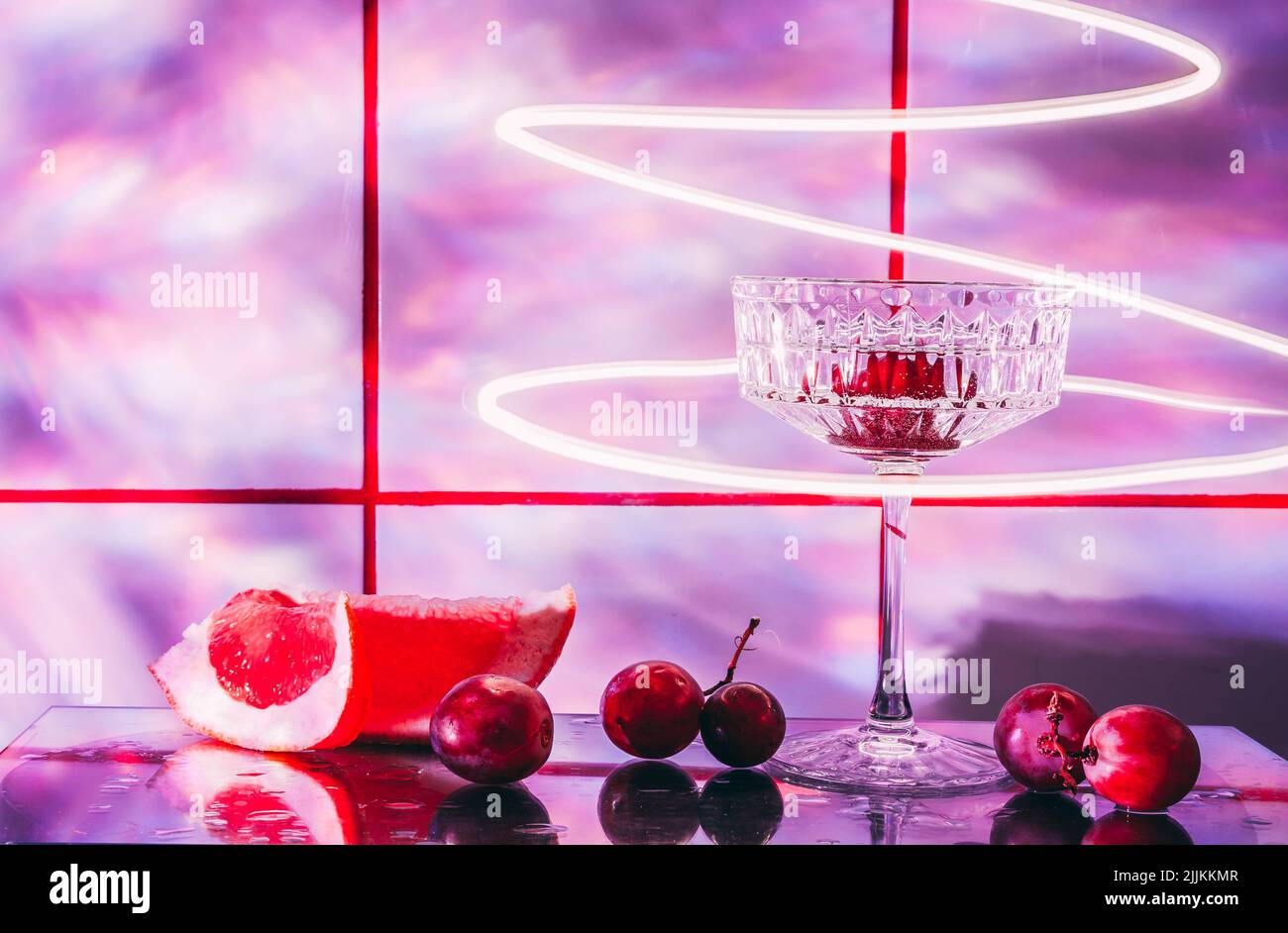 Crystal glass for cocktails on a glass surface. Fruits - grapes, grapefruit next to the glass. Abstract background. Stock Photo