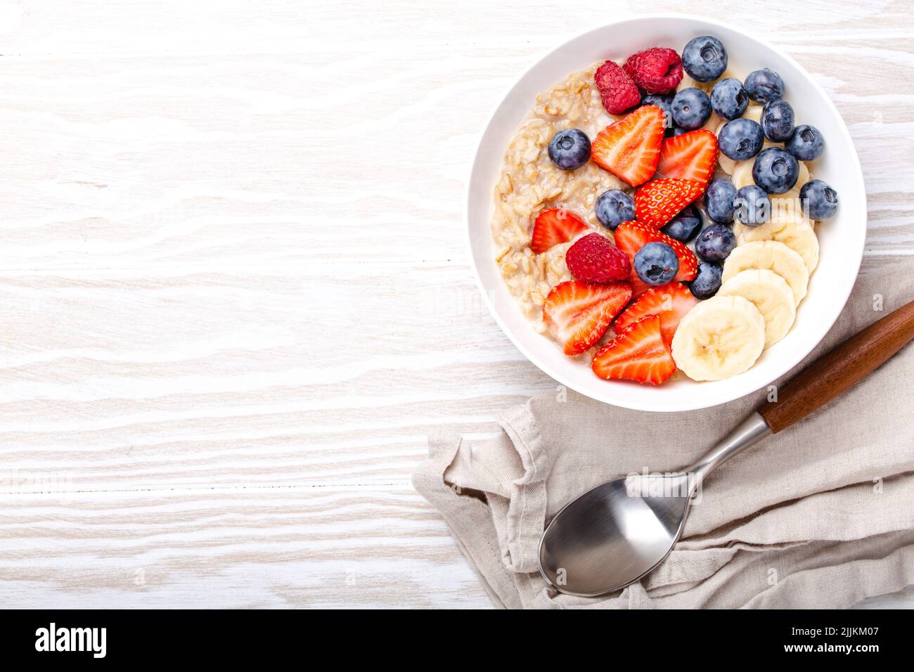 Oatmeal porridge with fruit and berries on white wooden table Stock Photo