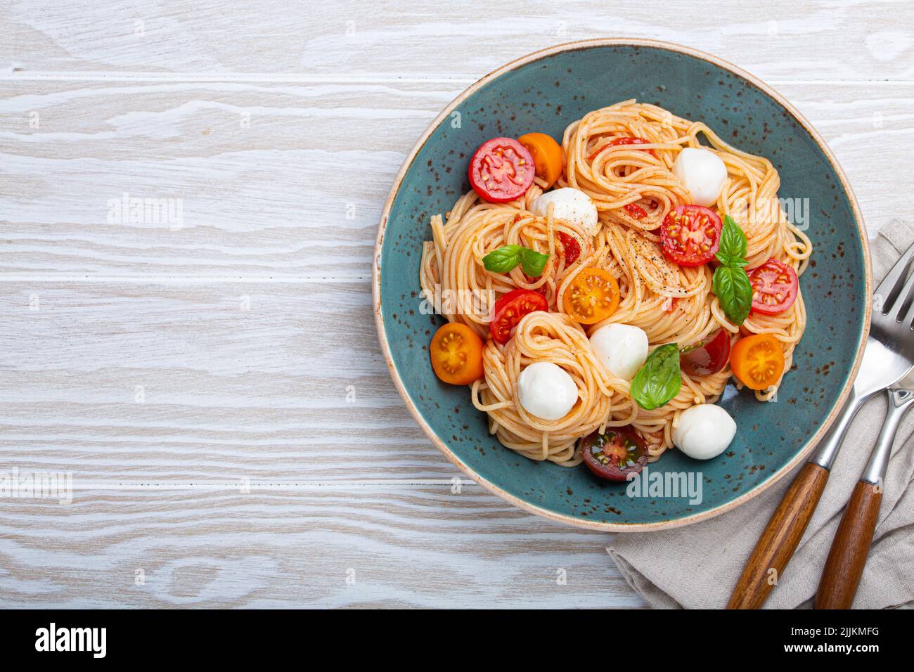 spaghetti with mozzarella, colourful cherry tomatoes, fresh basil on ceramic plate Stock Photo