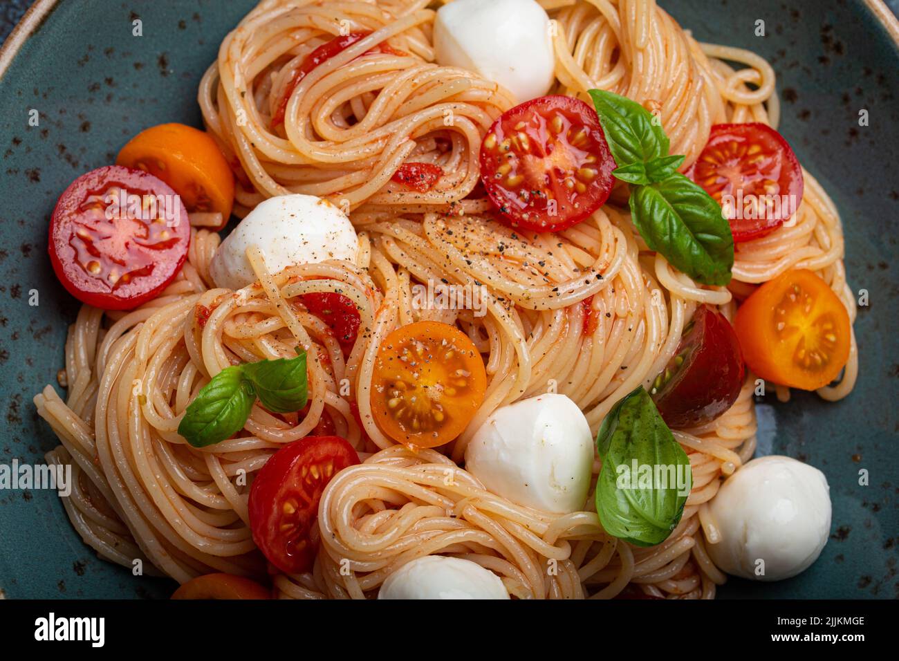 Spaghetti with mozzarella, colourful cherry tomatoes, fresh basil on ceramic plate Stock Photo