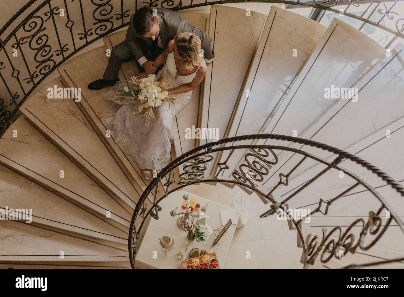 A top view of a Caucasian wedding couple sitting together on the spiral stairs, looking at each other Stock Photo