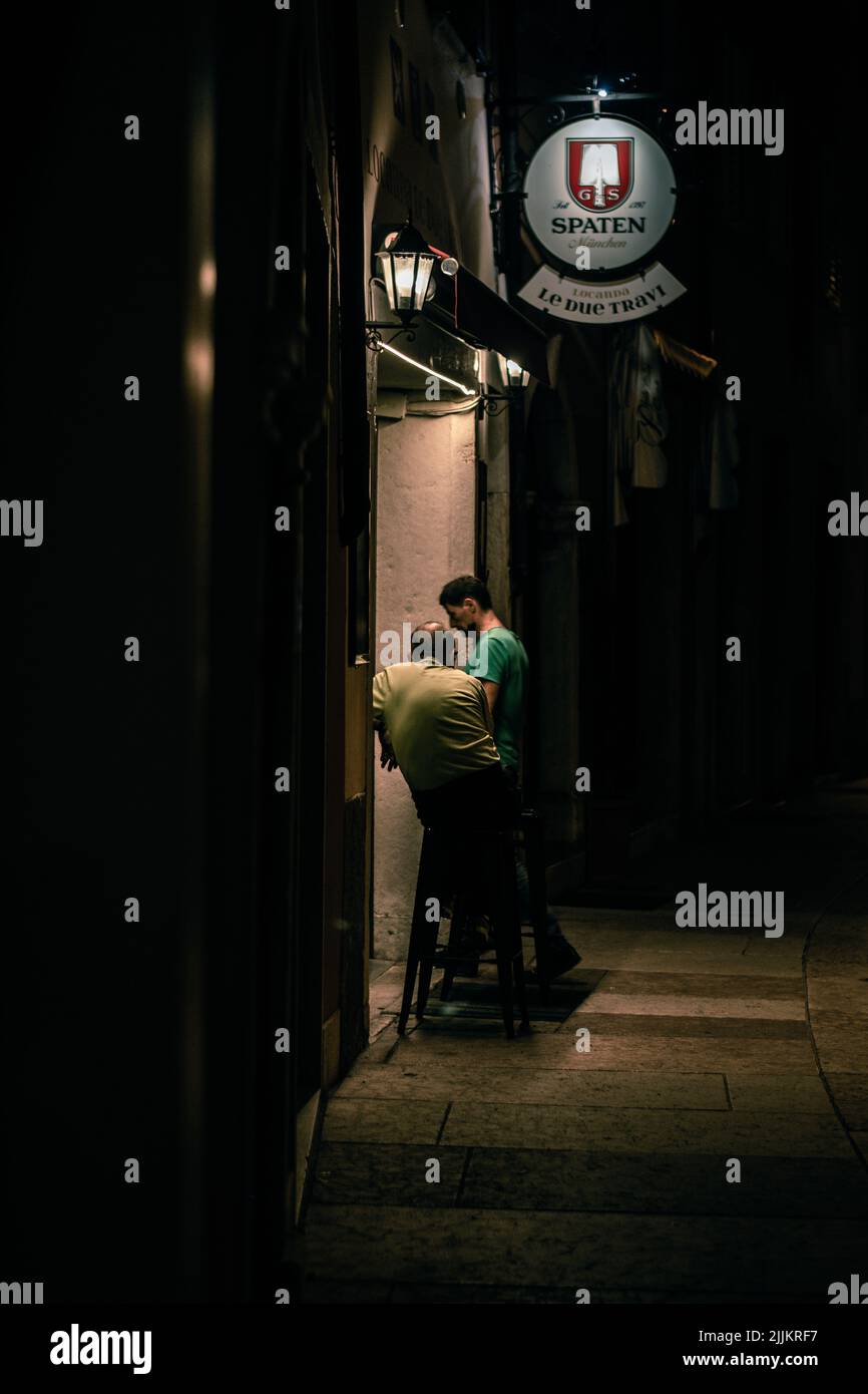 A vertical shot of two men standing outside a pub in the center of Trento, Italy at night Stock Photo