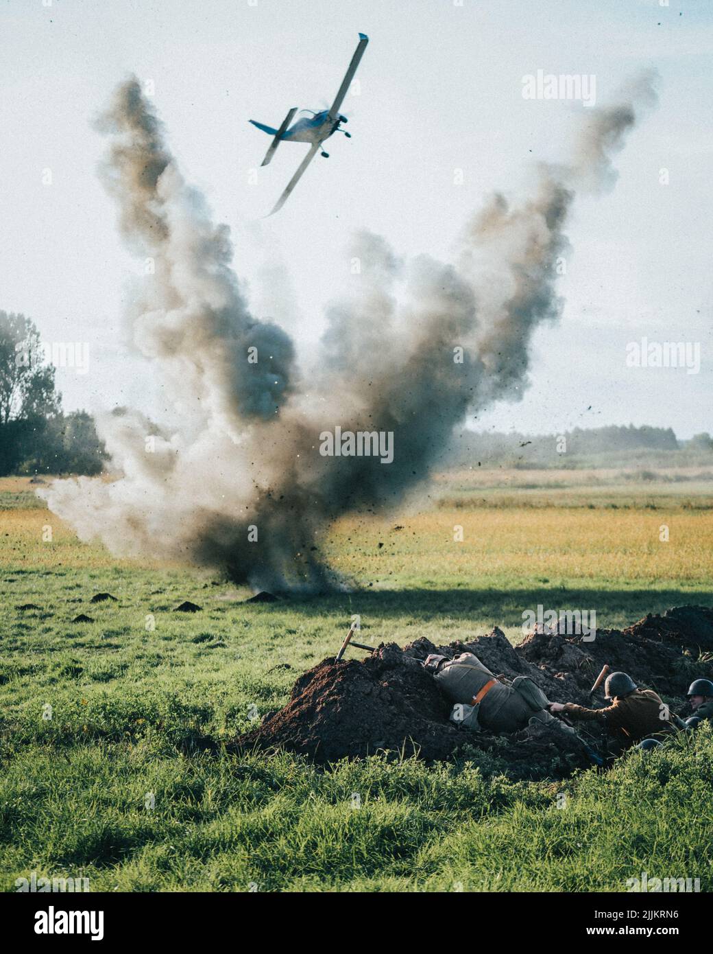 A World War 2 plane bombarding a green field with soldiers cowering in the trenches Stock Photo