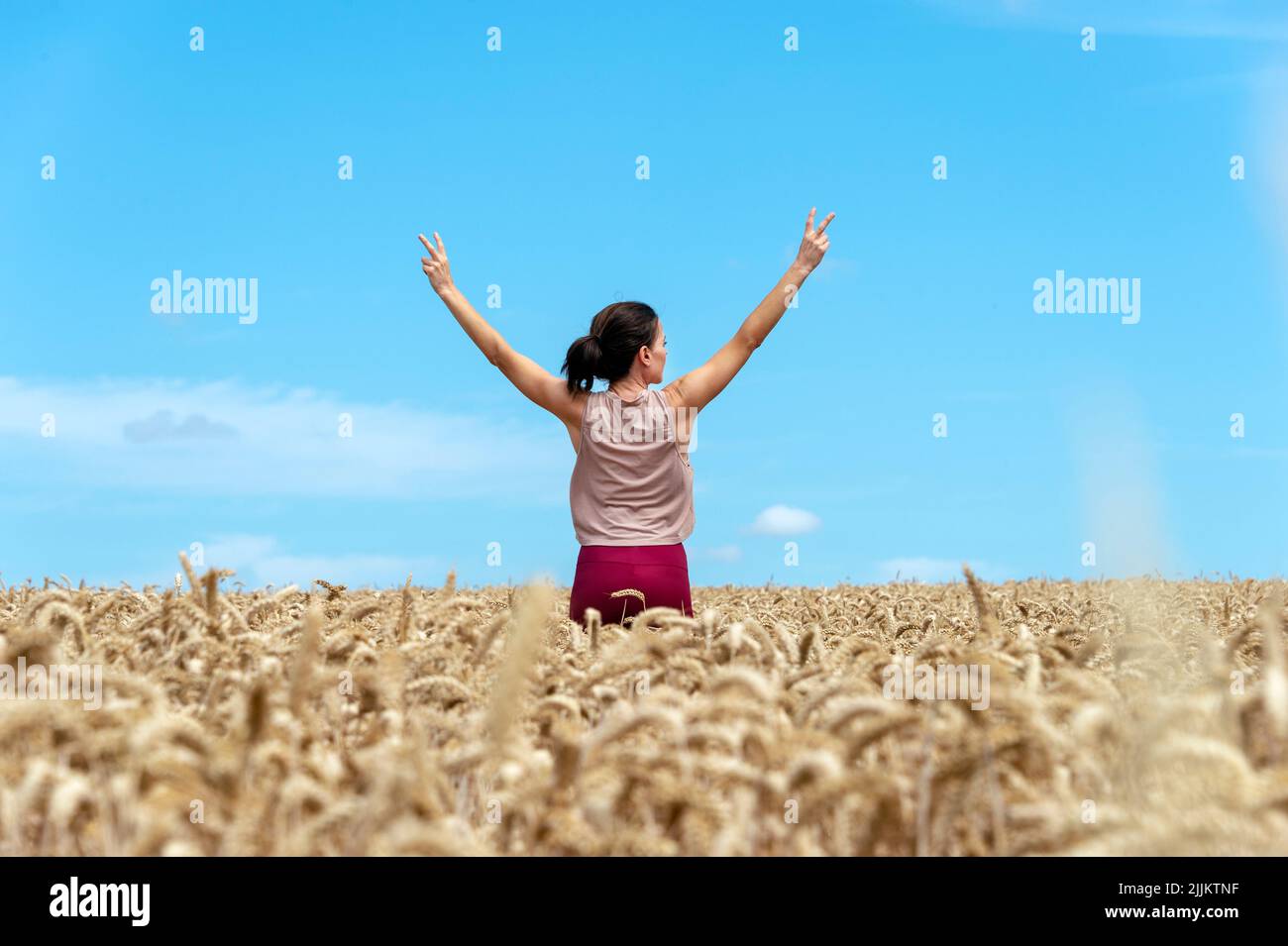 Happy woman feeling free with her arms outstretched, standing in a field of golden wheat Stock Photo
