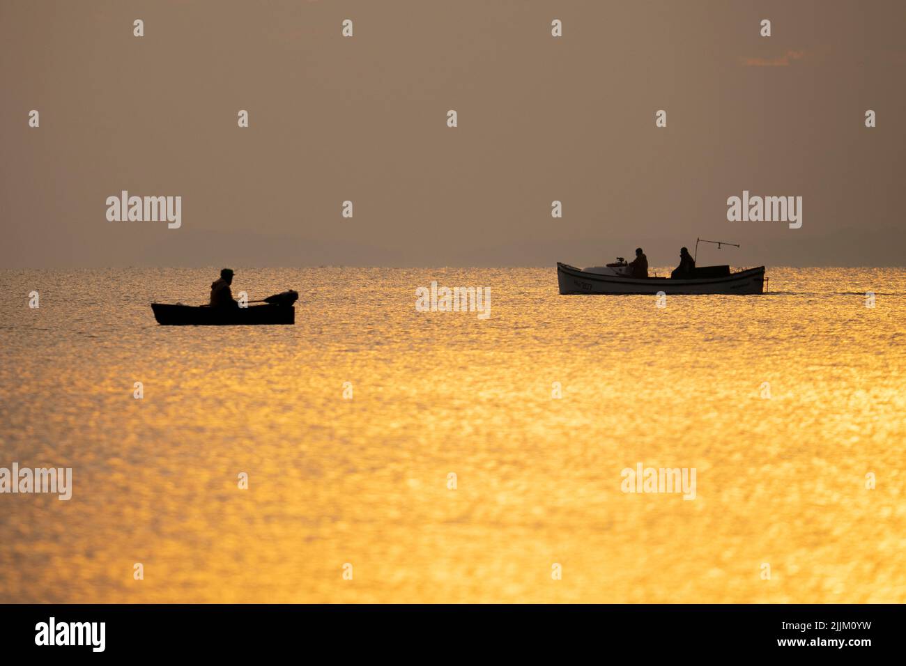 A scenery of silhouettes of boats with people in the calm sea at sunset ...