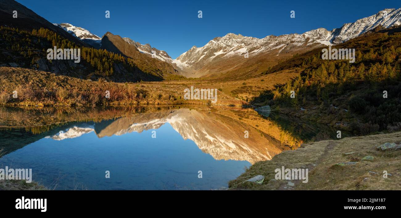 Reflection of autumn larch tree forest and mountain landscape in lake grundsee in wallis loetschental switzerland. Stock Photo