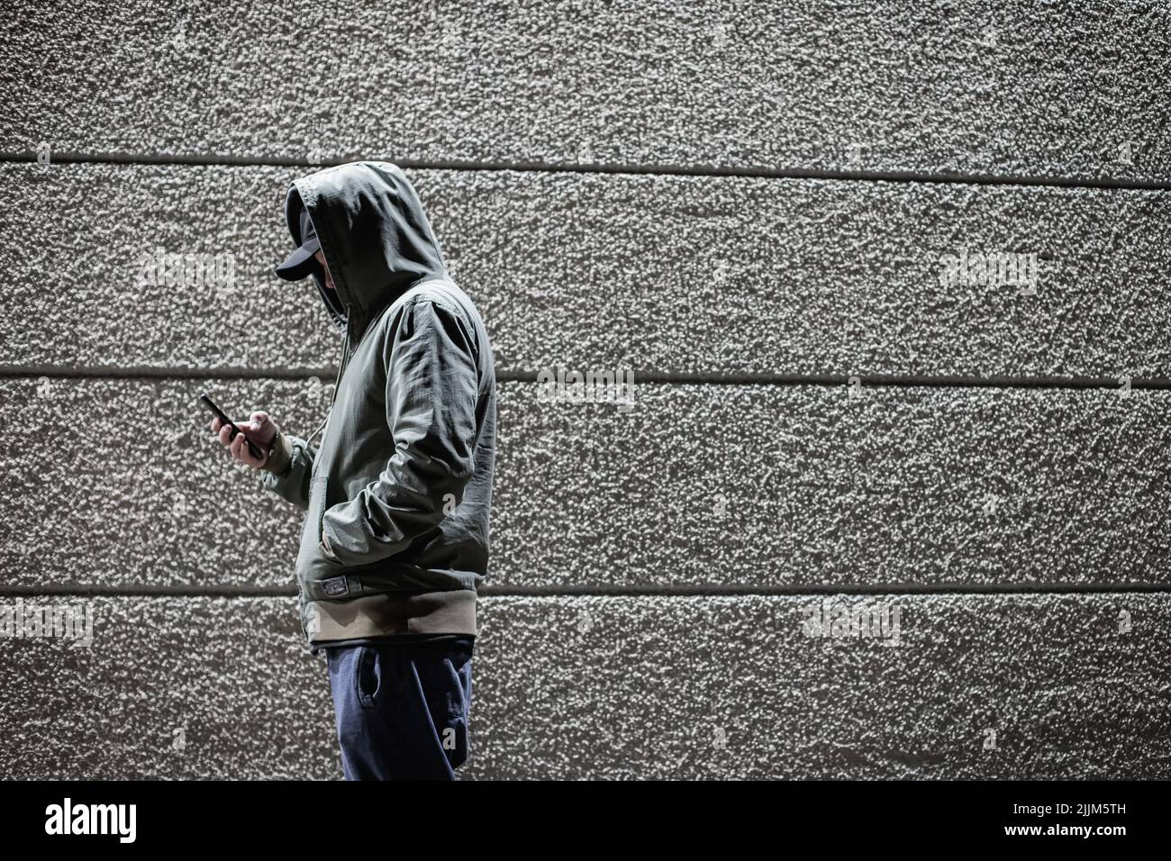 A side view of a person in an anorak holding his phone against a striped wall background Stock Photo