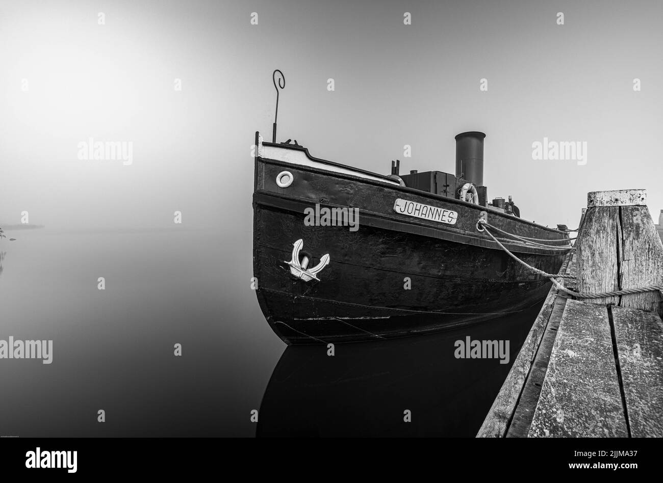 A grayscale of a boat moored at a dock against a foggy horizon Stock ...