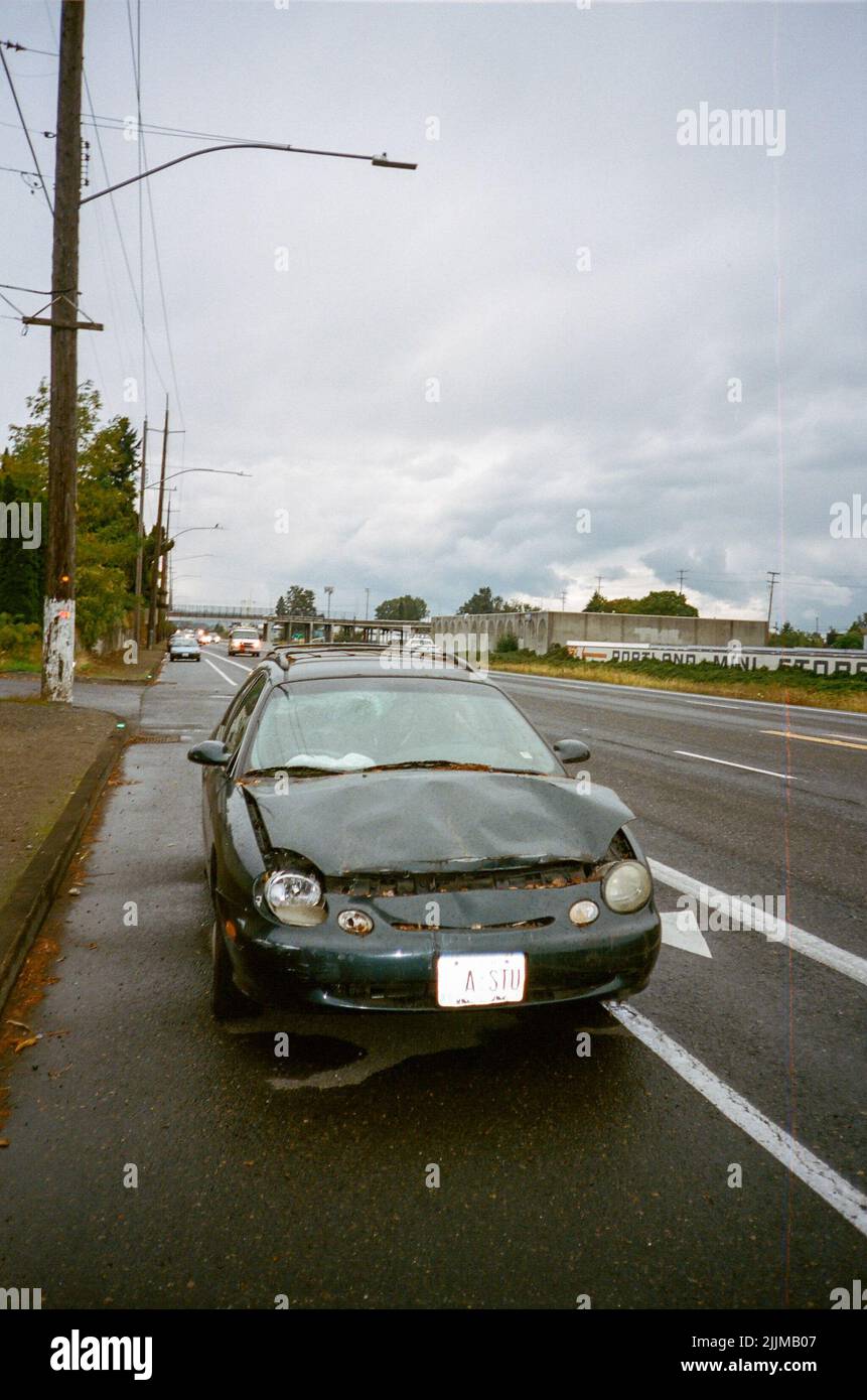 A vertical shot of a damaged Ford sedan on an industrial road Stock Photo