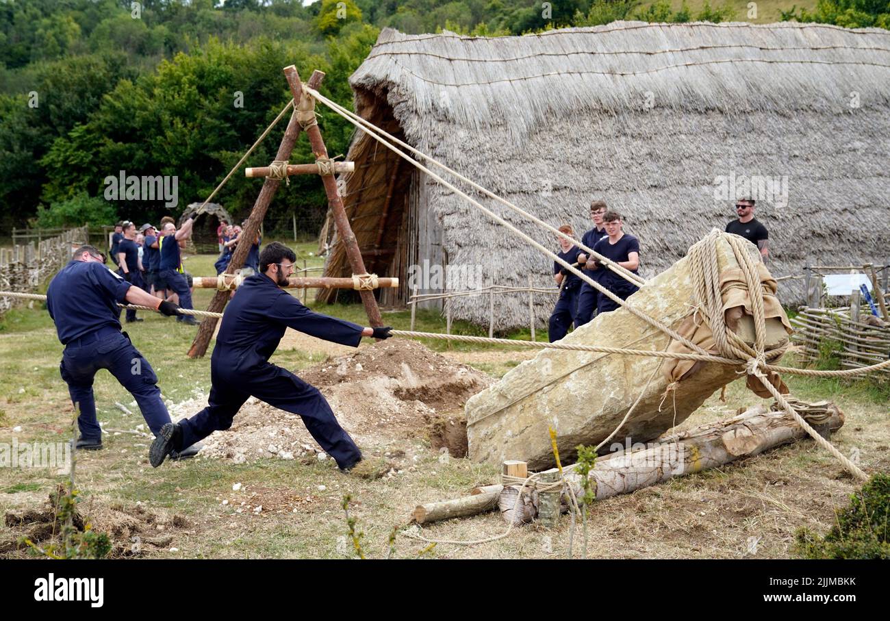 Crew members from HMS Queen Elizabeth and volunteers help move a 3.5 ton standing stone, using only traditional methods, at Butser Ancient Farm to mark its 50 year anniversary. Construction at the farm, which will be ongoing over the summer, based on excavations from Danebury Iron Age Hillfort near Andover, Hampshire, will test out new theories about how roundhouses may have been constructed and reflecting and continuing the pioneering work on roundhouse construction conducted at Butser during the 1970s. Picture date: Wednesday July 27, 2022. Stock Photo