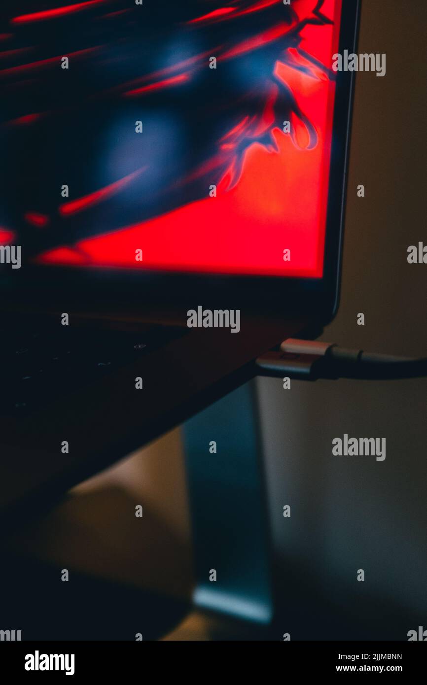 A vertical closeup of a laptop with a red neon wallpaper Stock Photo