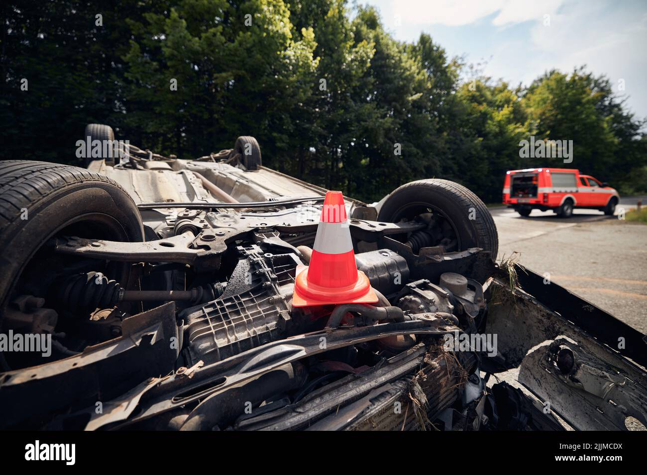 Damaged car on the roof after accident against fire rescue vehicle. Selective focus on traffic cone. Stock Photo